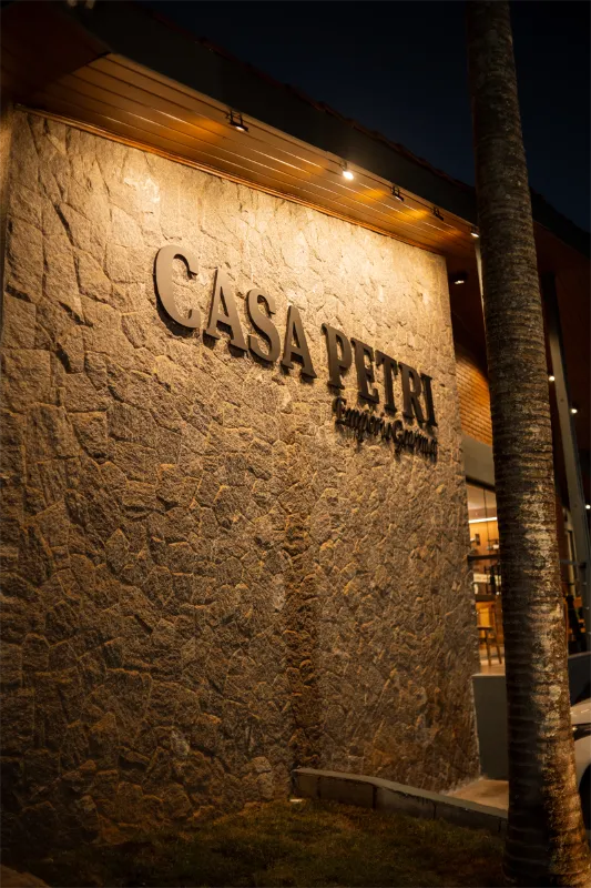 Detalhe da fachada de pedra com o letreiro Casa Petri iluminado