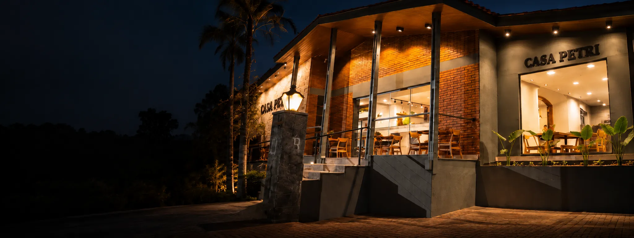 Fachada da Casa Petri iluminada à noite, com varanda e mesas para receber os visitantes